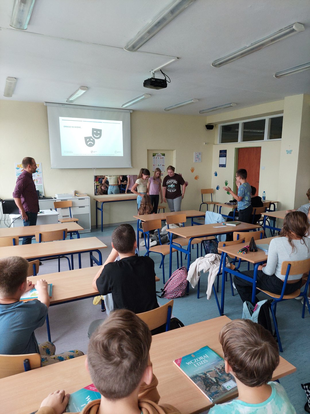 Dzieci siedzą w klasie, troje dzieci odgrywa scenkę teatralną