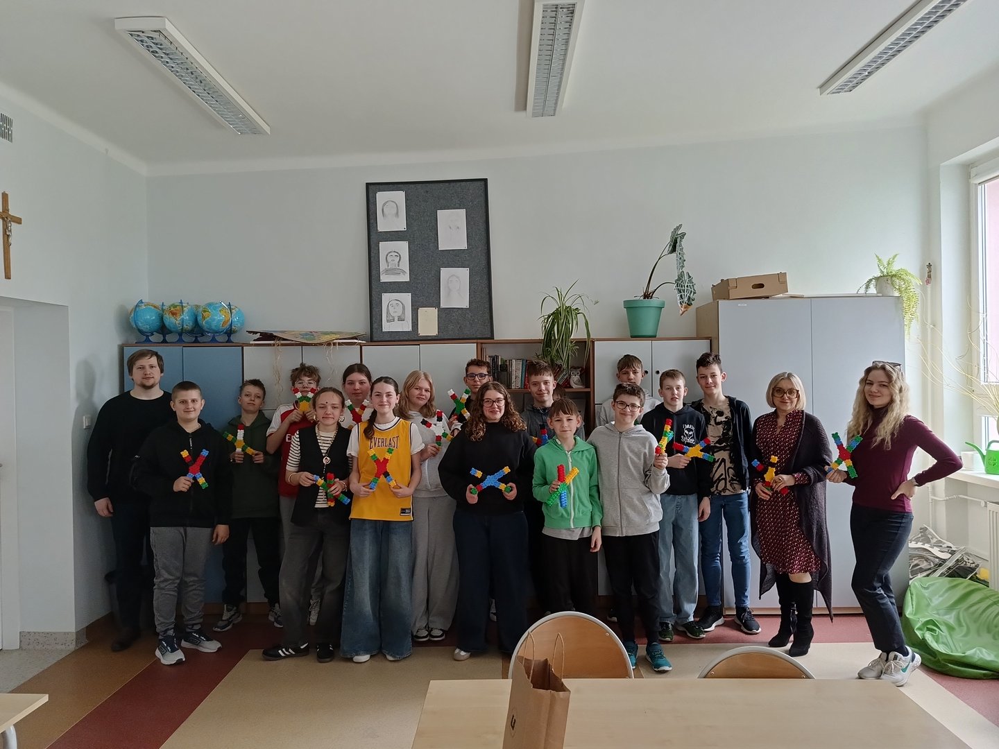 Dzieci stoją w grupie całą klasą i trzymają w dłoniach zrobione z klocków chromosomy.