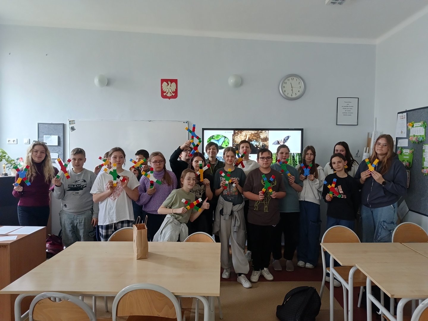 Dzieci stoją w grupie całą klasą i trzymają w dłoniach zrobione z klocków chromosomy.
