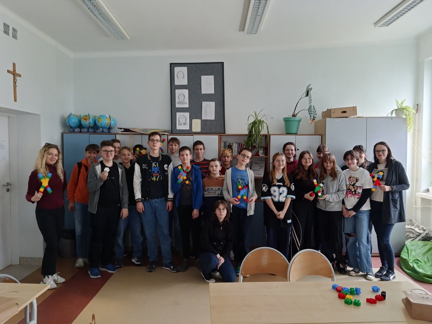 Dzieci stoją w grupie całą klasą i trzymają w dłoniach zrobione z klocków chromosomy.