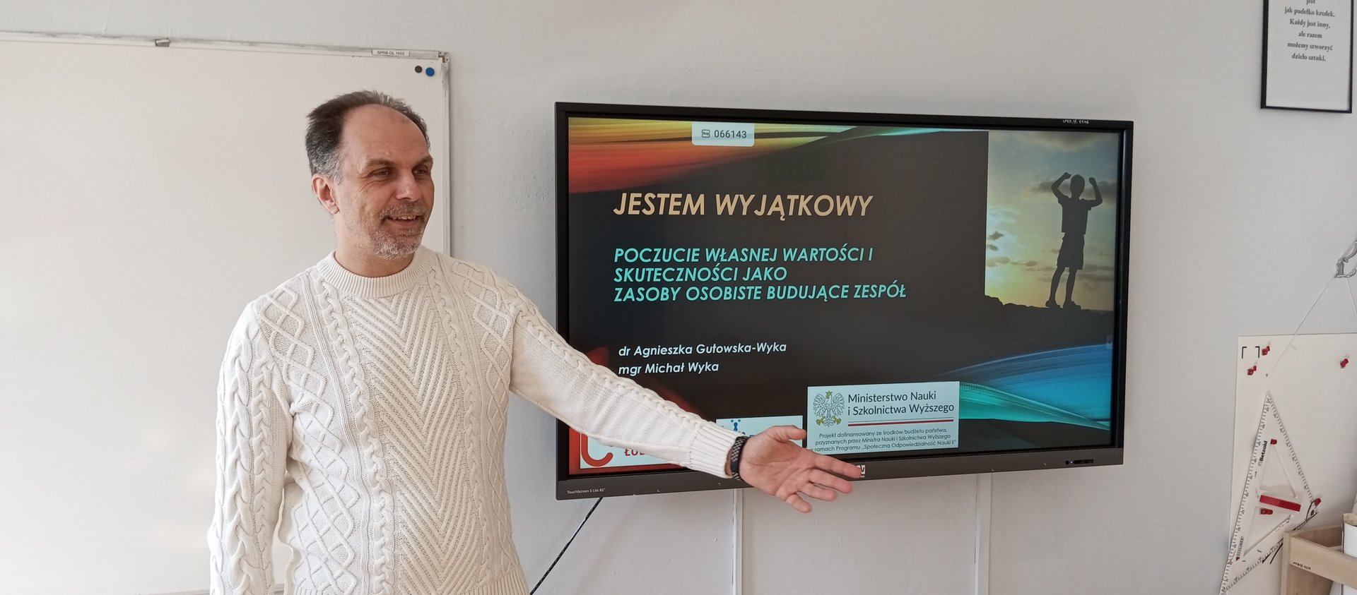 Prowadzący warsztat stoi przy ekranie zawieszonym przy ścianie podczas rozpoczęcia warsztatu.