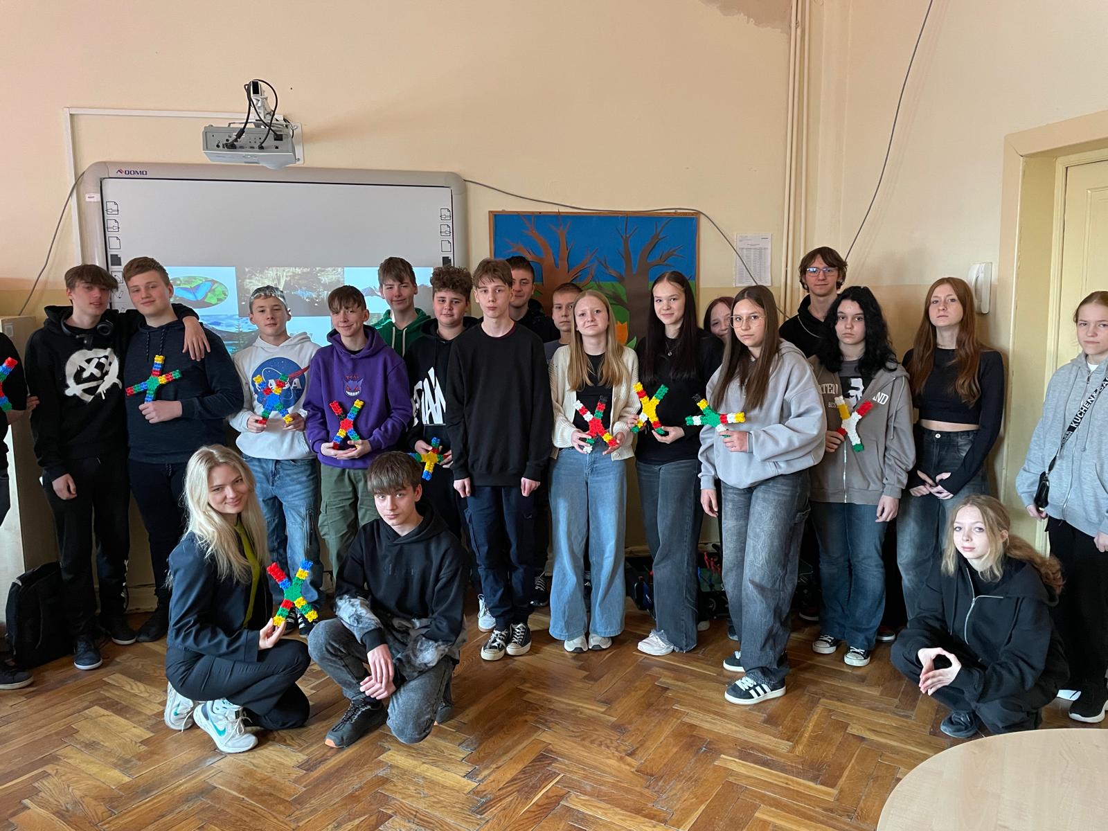 Dzieci stoją w zdjęciu grupowym po skończonym warsztacie i trzymają w dłoniach zbudowane przez siebie chromosomy z klocków